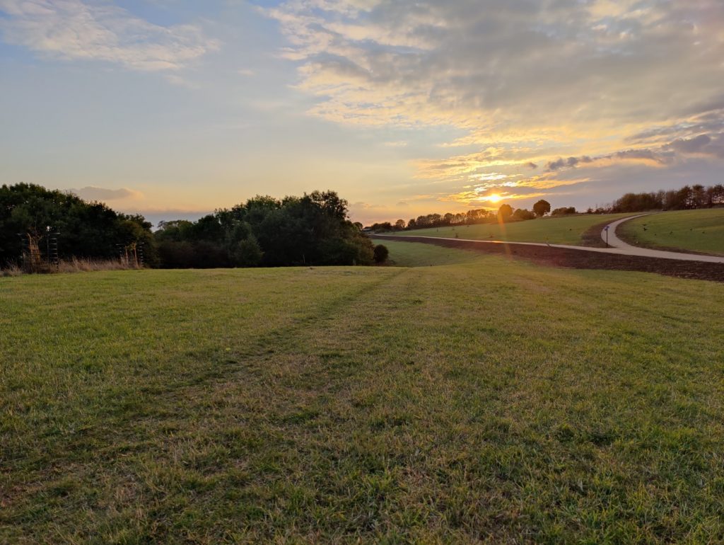 Landscape view showing grass parkland with trees, paths and the sunset in the distance